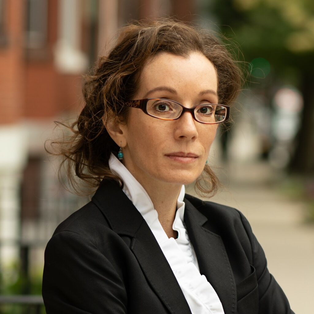 A portrait of a woman with shoulder-length wavy brown hair and eyeglasses. 2022 RCP Network Gathering Speakers.